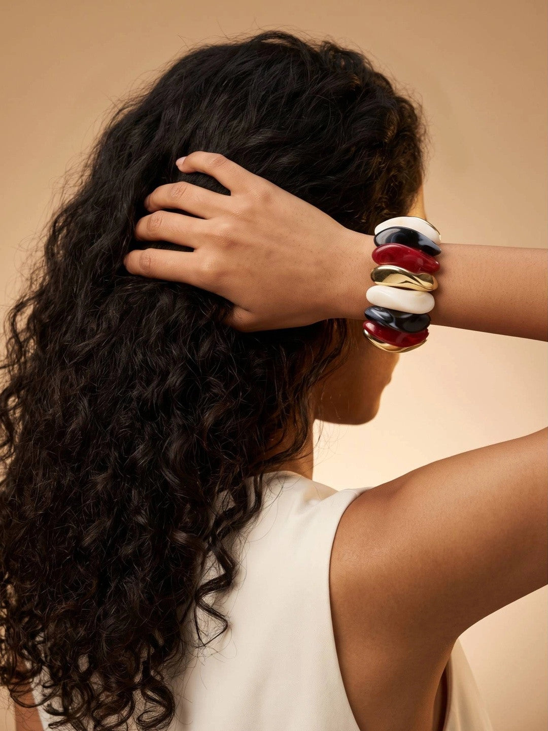 Woman wearing chunky multicolour resin cuff bracelet on her wrist while posing with hand in dark curly hair