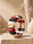 Multicolour resin cuff bracelet with red, black, ivory, and gold-tone tiles displayed upright on a travertine pedestal