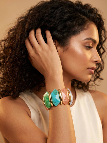 Model wearing multicolour resin stretch bracelet on wrist with hand raised near hair against warm backdrop
