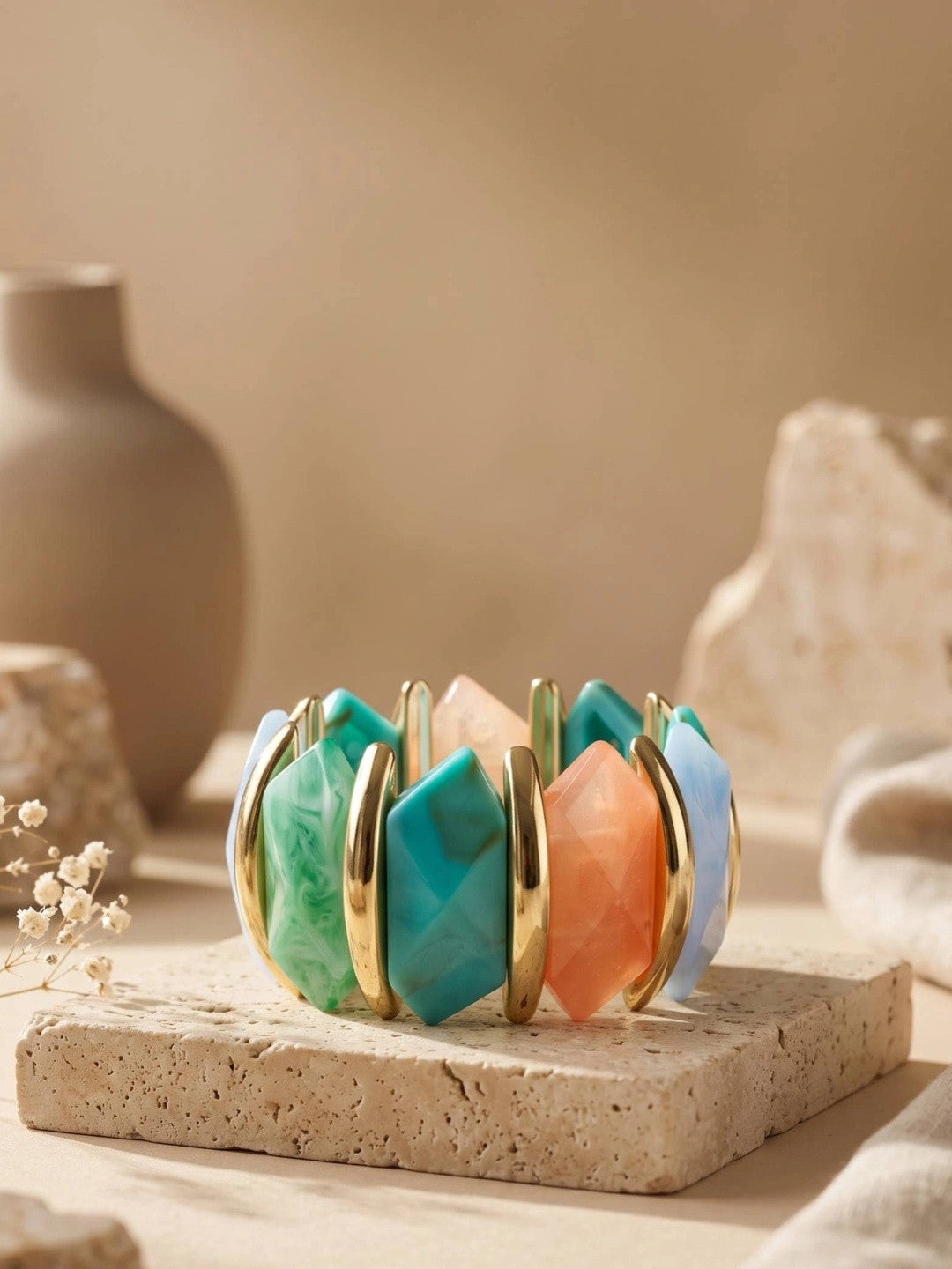 Multicolour resin stretch bracelet displayed on travertine block with beige vase and dried florals behind