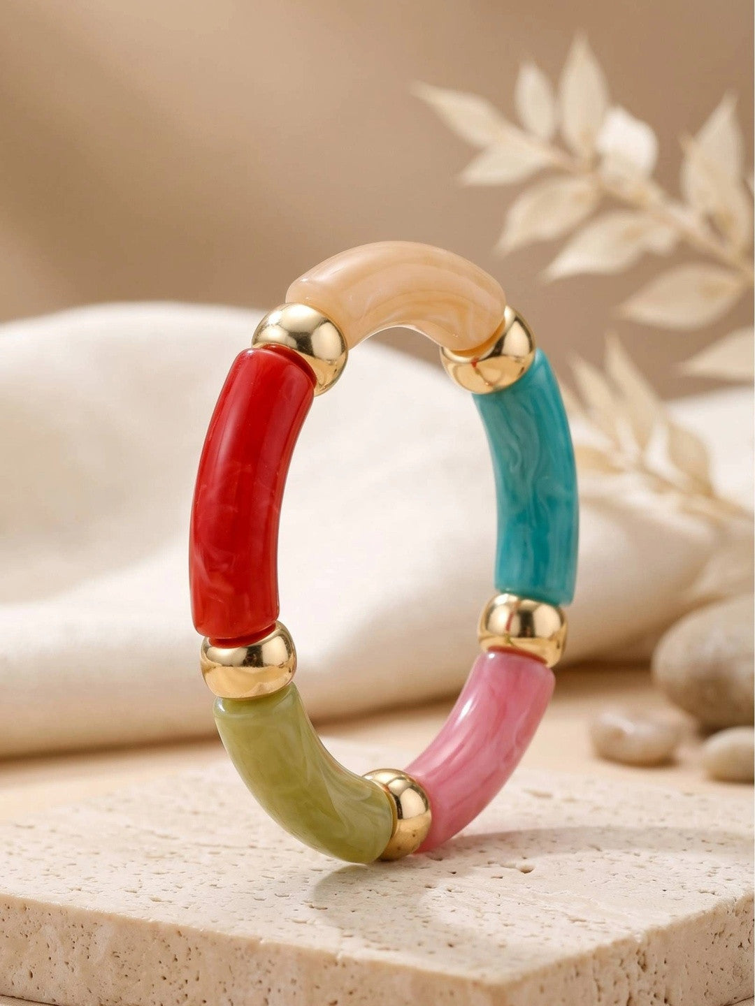 Close-up of multicolour marble resin tube bracelet propped upright on a neutral stone surface