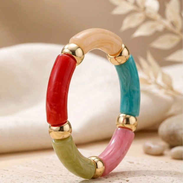 Close-up of multicolour marble resin tube bracelet propped upright on a neutral stone surface