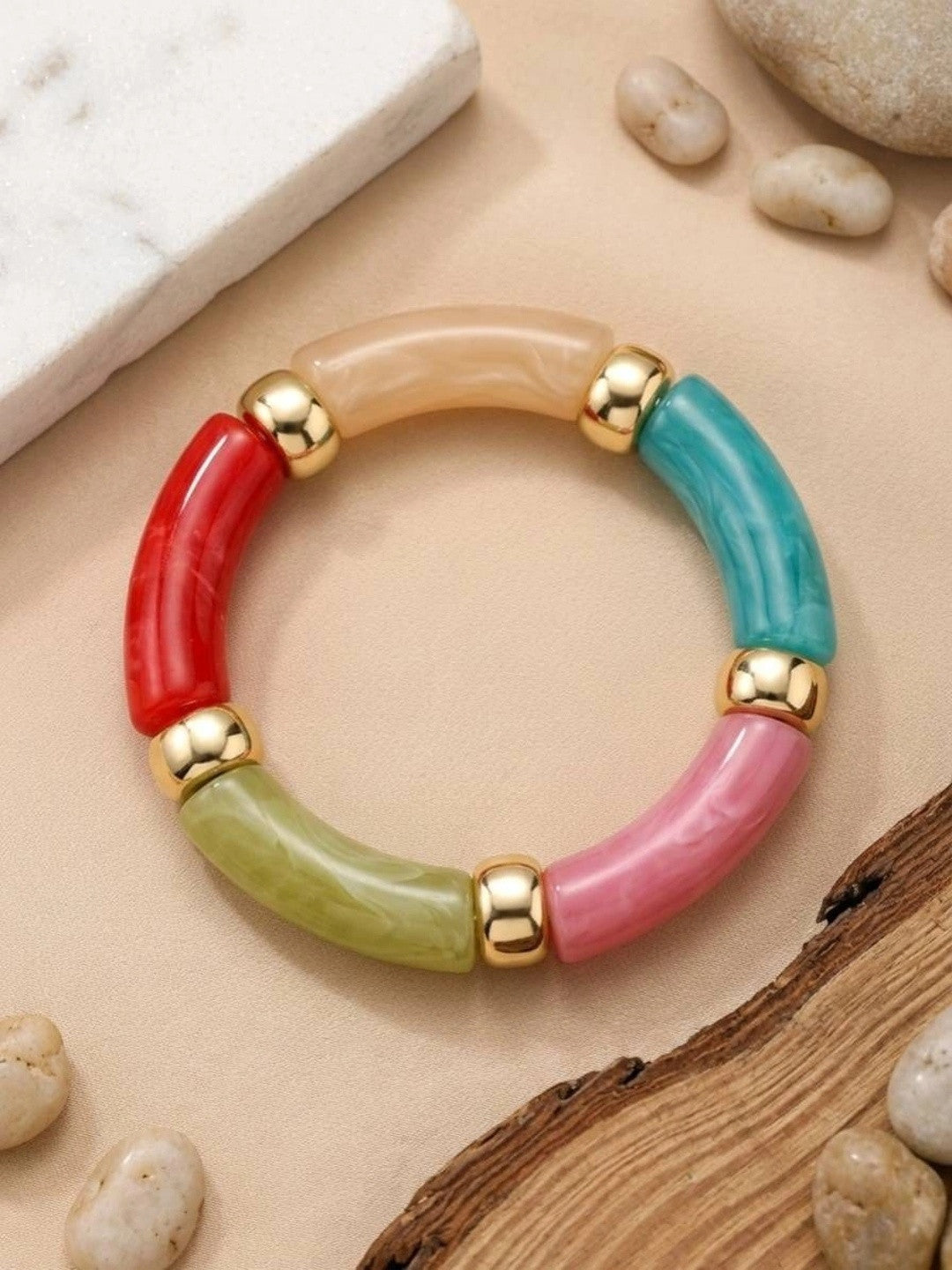 Flat top-down view of multicolour resin tube bracelet laid on a beige surface with pebbles