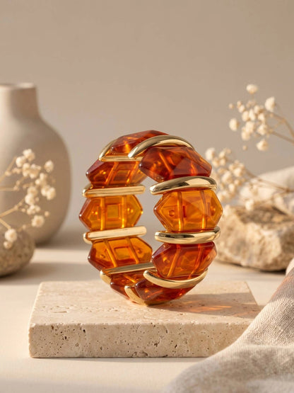 Faceted amber resin gold cuff bracelet displayed upright on a travertine block with dried florals