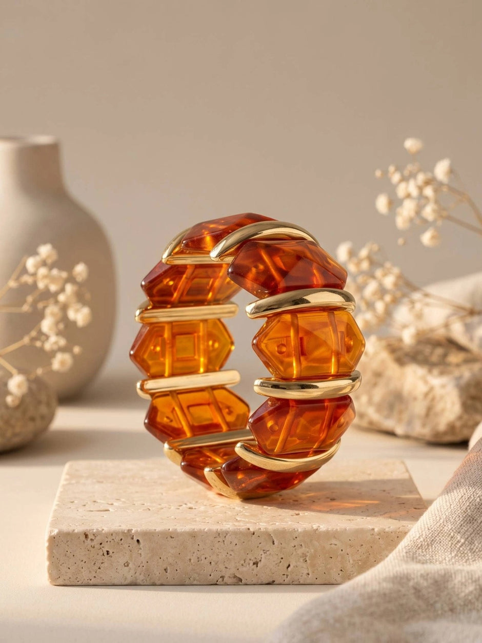 Faceted amber resin gold cuff bracelet displayed upright on a travertine block with dried florals