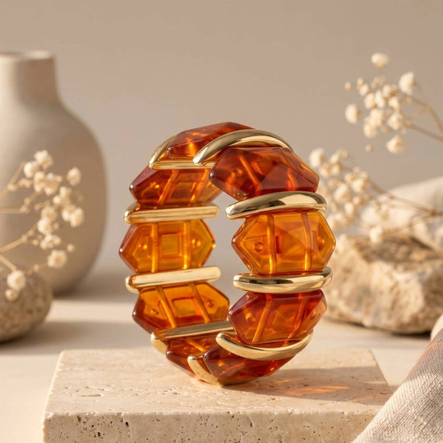 Faceted amber resin gold cuff bracelet displayed upright on a travertine block with dried florals