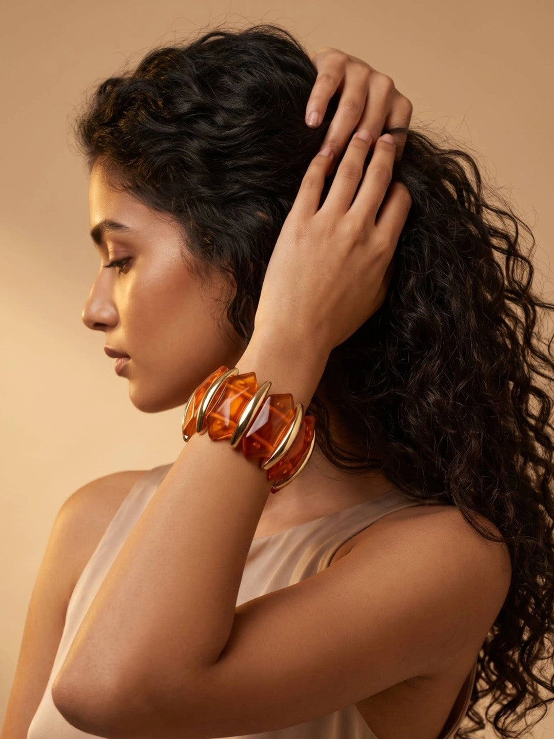 Model wearing amber resin gold-toned cuff bracelet on raised wrist against warm beige background