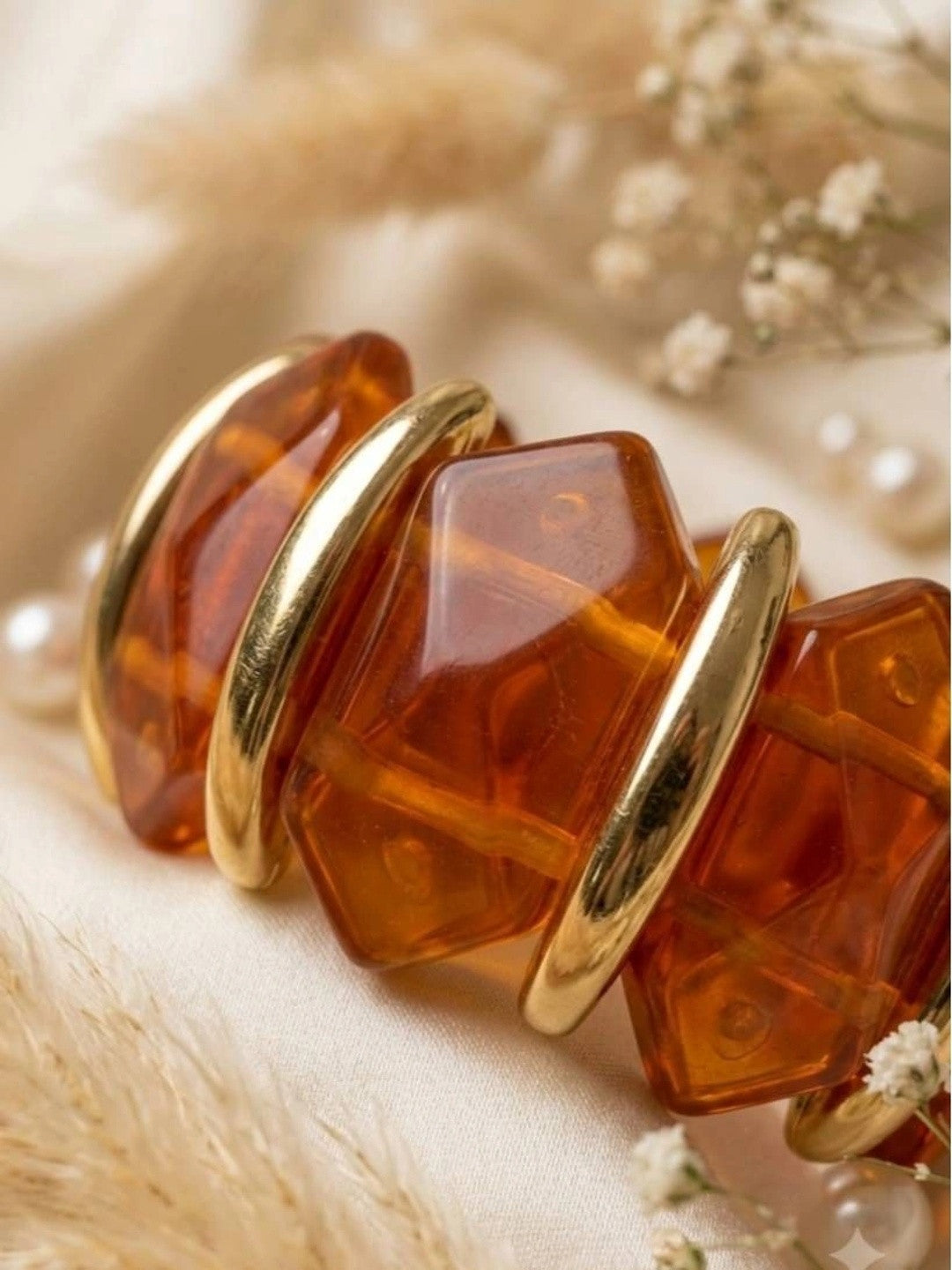 Close-up of faceted cognac resin stones separated by curved gold-toned metal arches on bracelet
