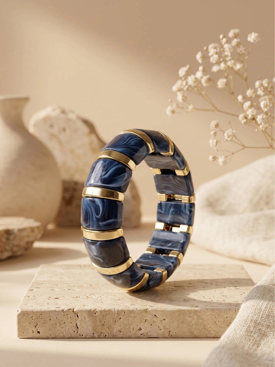 Navy blue marble resin bracelet standing upright on a travertine tile surface styled with dried gypsophila and a ceramic vase