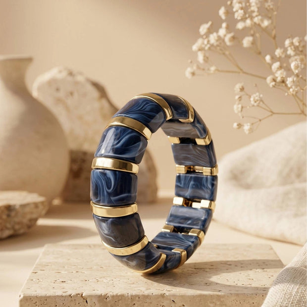 Navy blue marble resin bracelet standing upright on a travertine tile surface styled with dried gypsophila and a ceramic vase