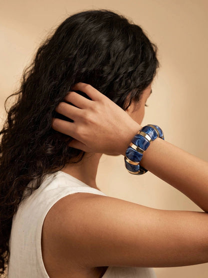 Navy blue marble resin stretch bracelet worn on the wrist of a woman in a white sleeveless top with long curly hair