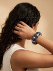 Navy blue marble resin stretch bracelet worn on the wrist of a woman in a white sleeveless top with long curly hair