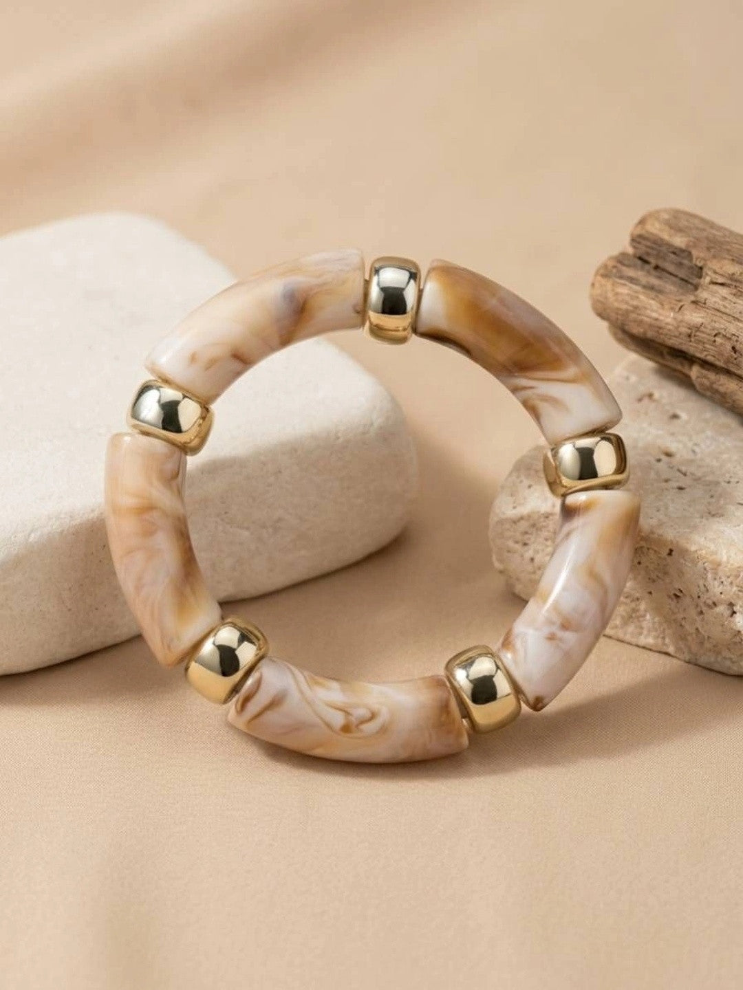 Top-down view of marble resin tube bead bracelet with gold-tone spacers displayed on smooth white pebbles