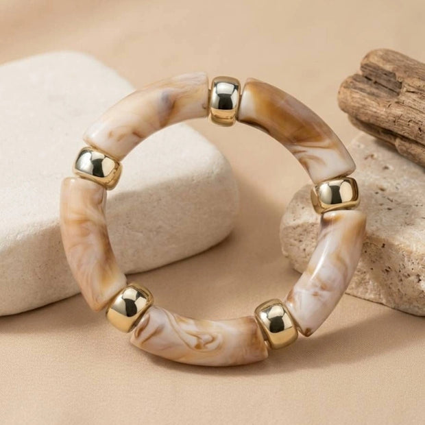 Top-down view of marble resin tube bead bracelet with gold-tone spacers displayed on smooth white pebbles