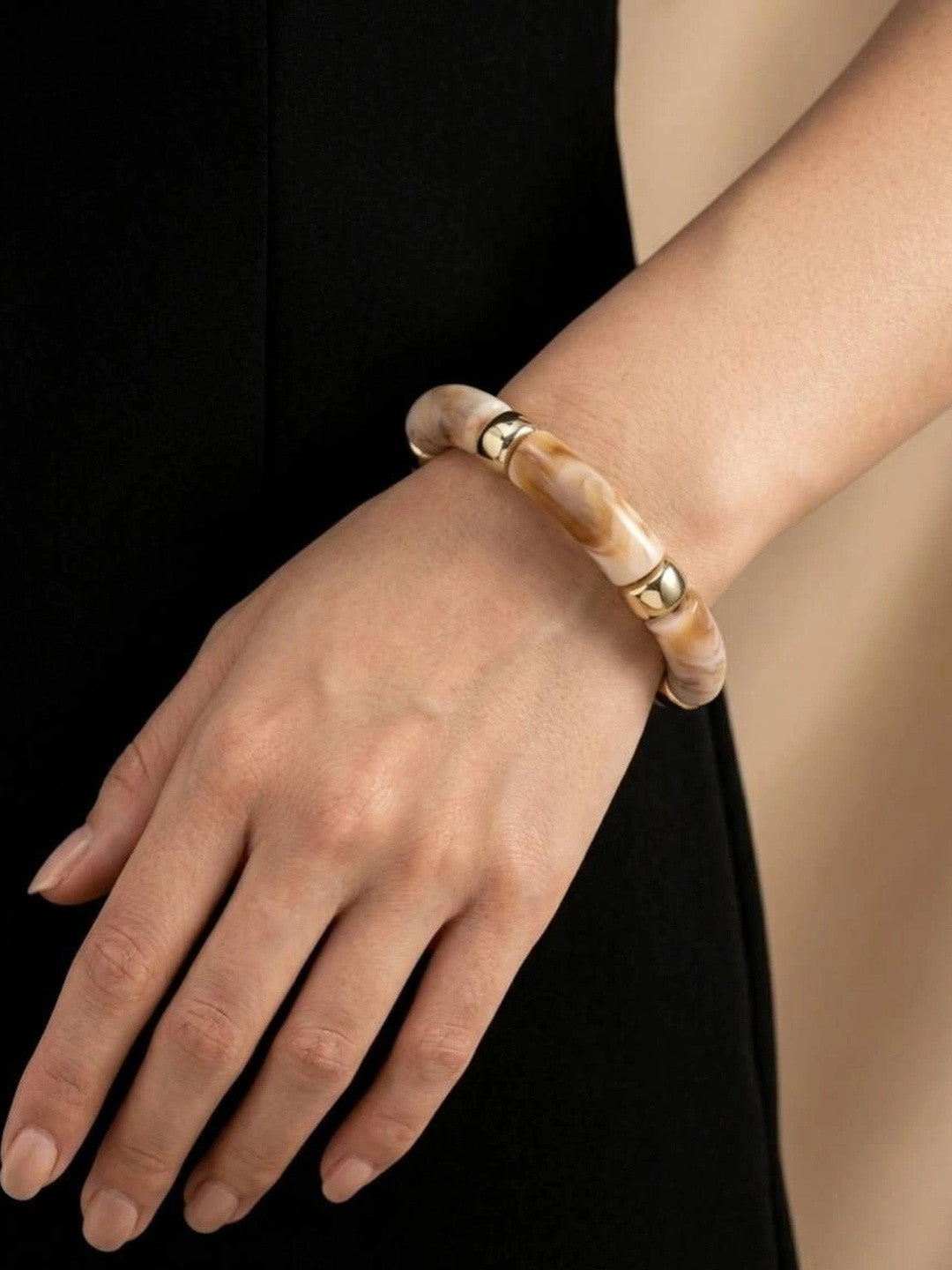 Marble resin gold-tone bracelet worn on a woman's wrist against a black outfit