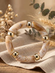 Cream and caramel marble resin bracelet with gold-tone beads laid on linen cloth with dried botanicals
