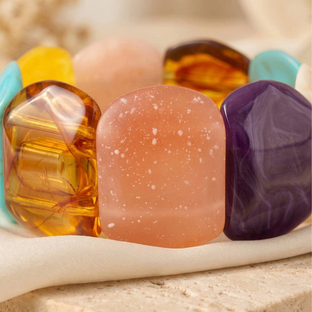 Close-up of multicolour resin bracelet showing translucent amber, frosted rose and marbled violet stones on a cream fabric surface