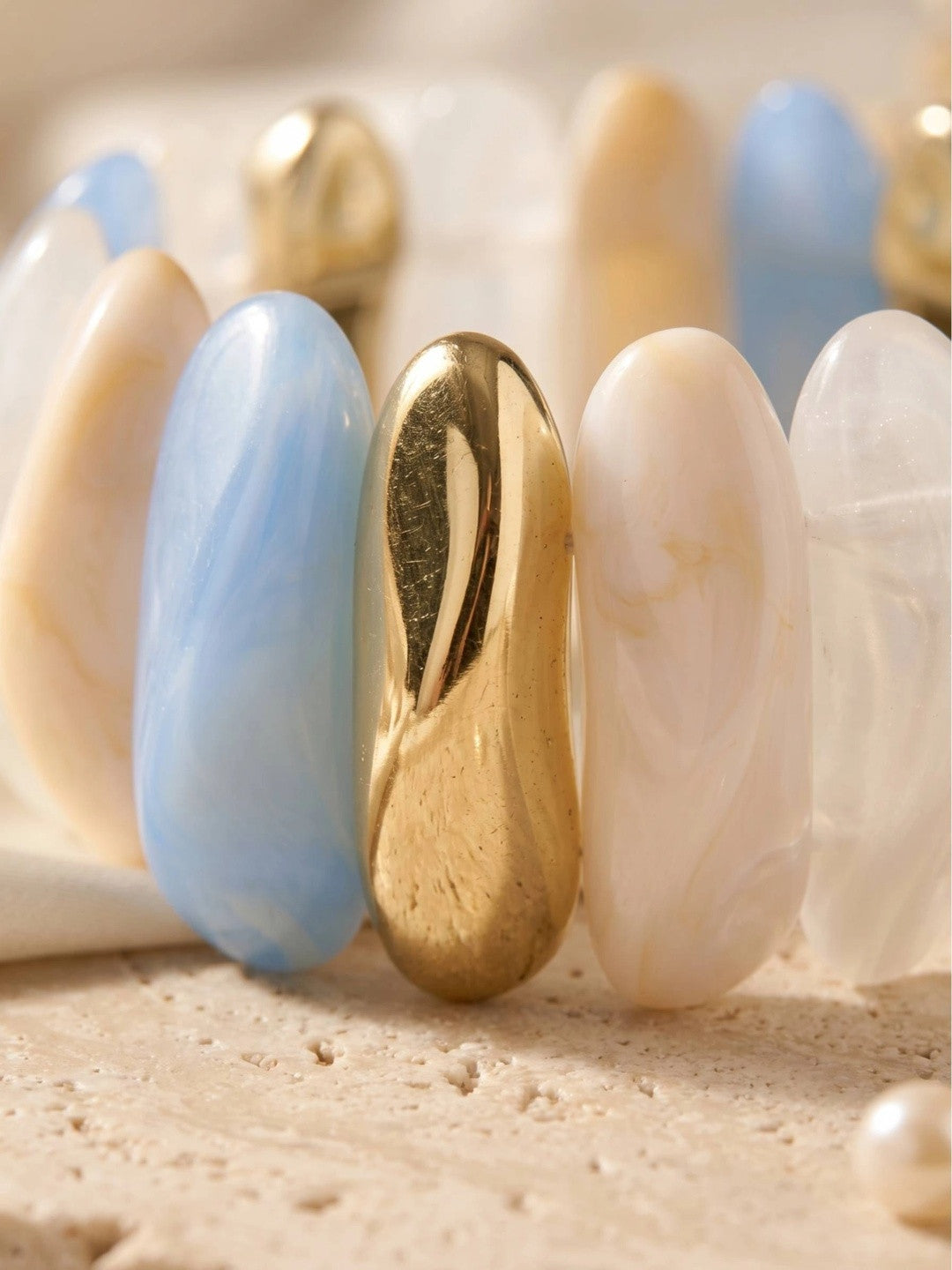 Close-up of sky blue cream and polished gold-tone oval resin segments on stretch bracelet laid flat