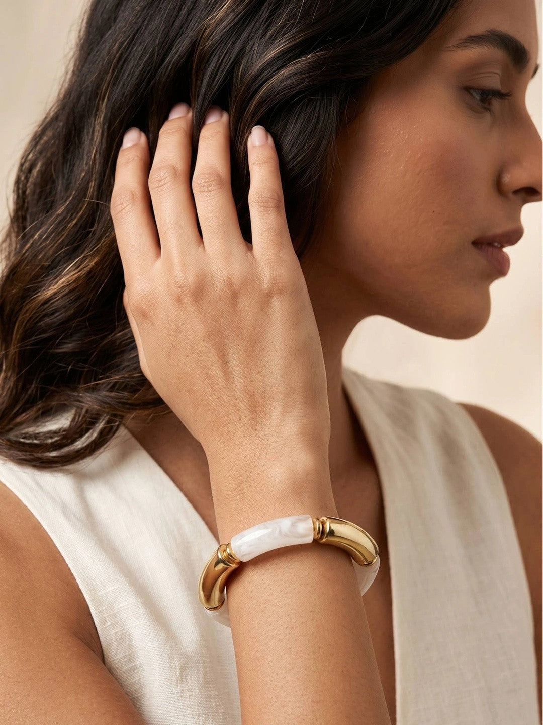 Woman wearing a gold and white resin cuff bracelet on her wrist, dressed in a white sleeveless top