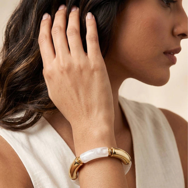 Woman wearing a gold and white resin cuff bracelet on her wrist, dressed in a white sleeveless top