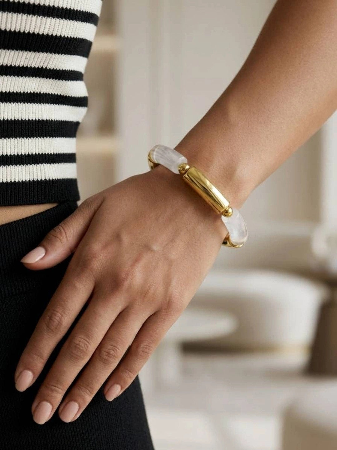 Close-up of a gold and white resin tube stretch bracelet worn on a wrist against a black and white striped top