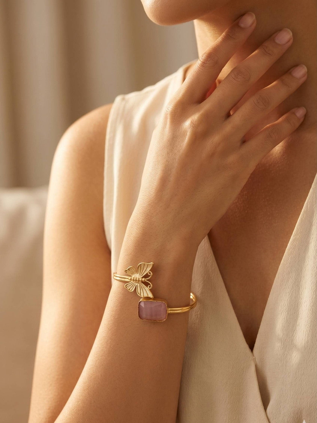 Woman wearing gold butterfly cuff bracelet on wrist dressed in cream sleeveless top in soft natural light