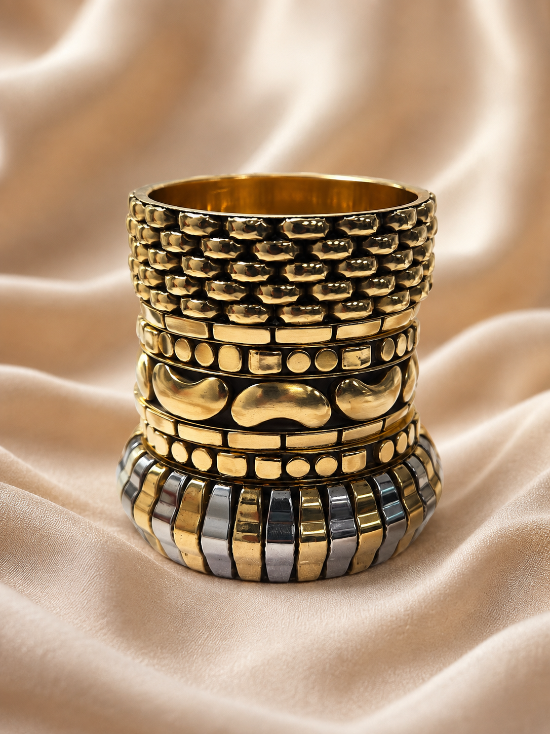 Five gold-tone bangles stacked vertically on cream satin revealing honeycomb, beaded and two-tone ribbed designs