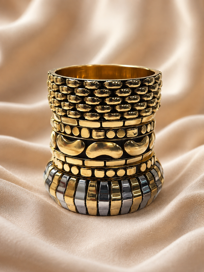 Five gold-tone bangles stacked vertically on cream satin revealing honeycomb, beaded and two-tone ribbed designs
