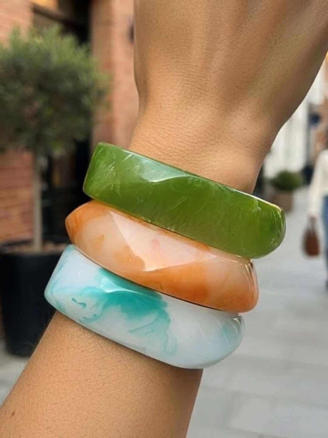 Three stacked marble resin bangles in green, orange and aqua blue worn on a wrist outdoors