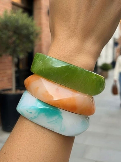 Three stacked marble resin bangles in green, orange and aqua blue worn on a wrist outdoors