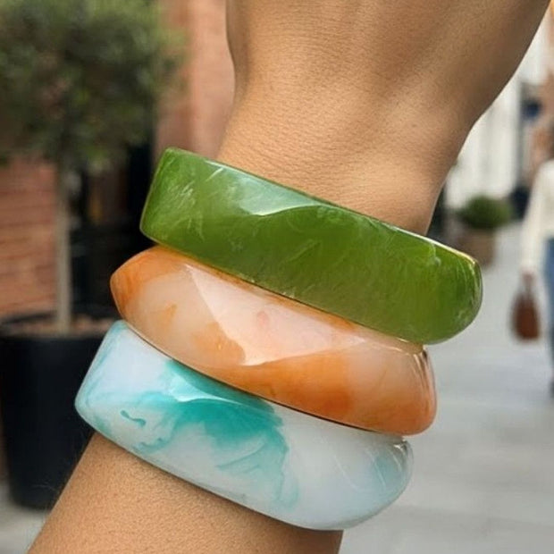 Three stacked marble resin bangles in green, orange and aqua blue worn on a wrist outdoors