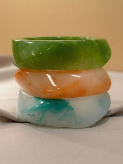 Set of three polished marble resin bangles stacked on a white ceramic surface against a beige background