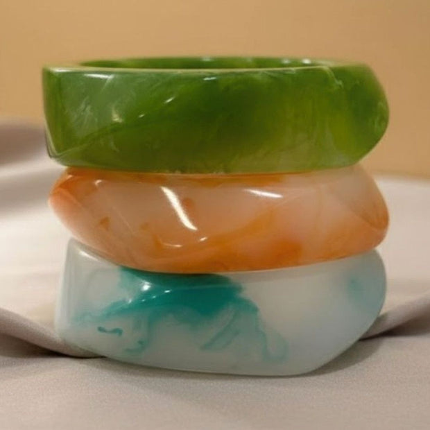 Set of three polished marble resin bangles stacked on a white ceramic surface against a beige background