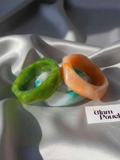 Green, orange and aqua marble resin bangles arranged on white satin fabric with The Glam Pouch branding card