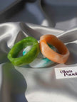 Green, orange and aqua marble resin bangles arranged on white satin fabric with The Glam Pouch branding card