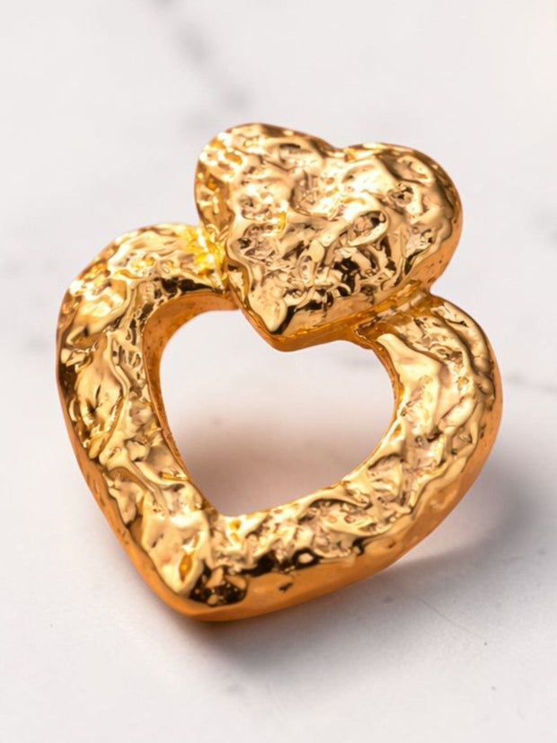 Single gold-toned double heart drop earring with hammered finish resting on a white marble surface