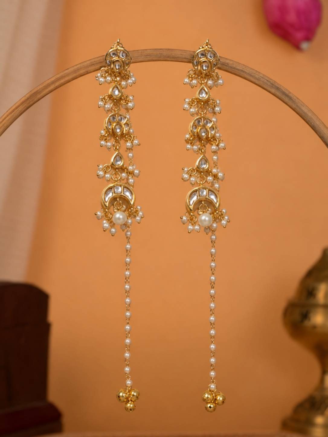 Pair of gold-plated kundan chandbali earrings with pearl chain drops hanging on a wooden display stand