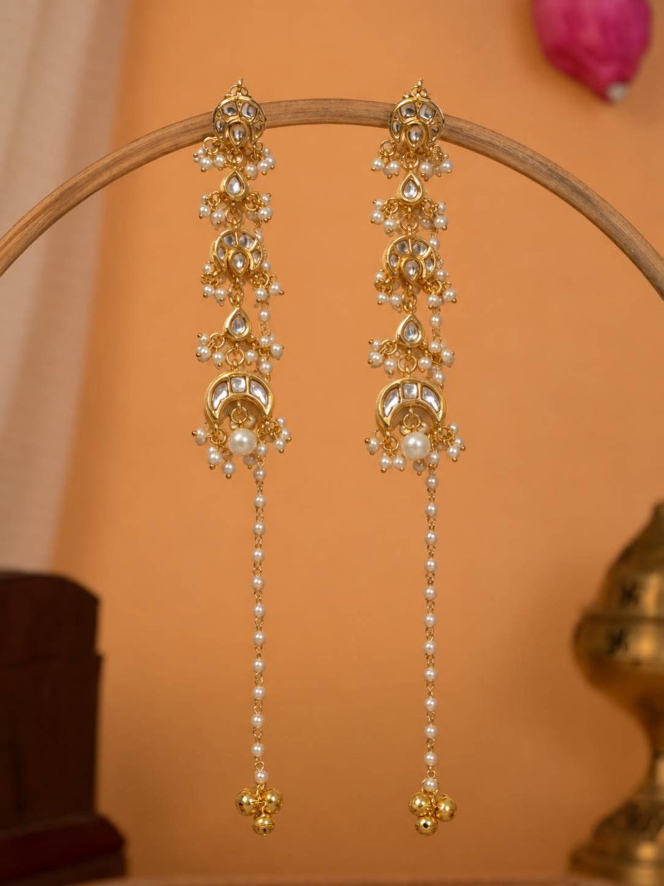 Pair of gold-plated kundan chandbali earrings with pearl chain drops hanging on a wooden display stand