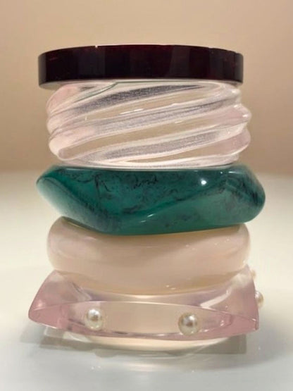 Five resin bangles stacked vertically showing teal marble, blush pearl, ivory, ribbed clear and tortoiseshell finishes