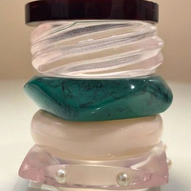 Five resin bangles stacked vertically showing teal marble, blush pearl, ivory, ribbed clear and tortoiseshell finishes