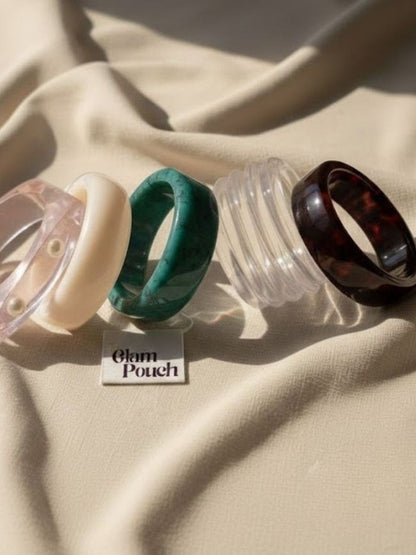 Five individual resin bangles laid flat on cream fabric next to a Glam Pouch branded card