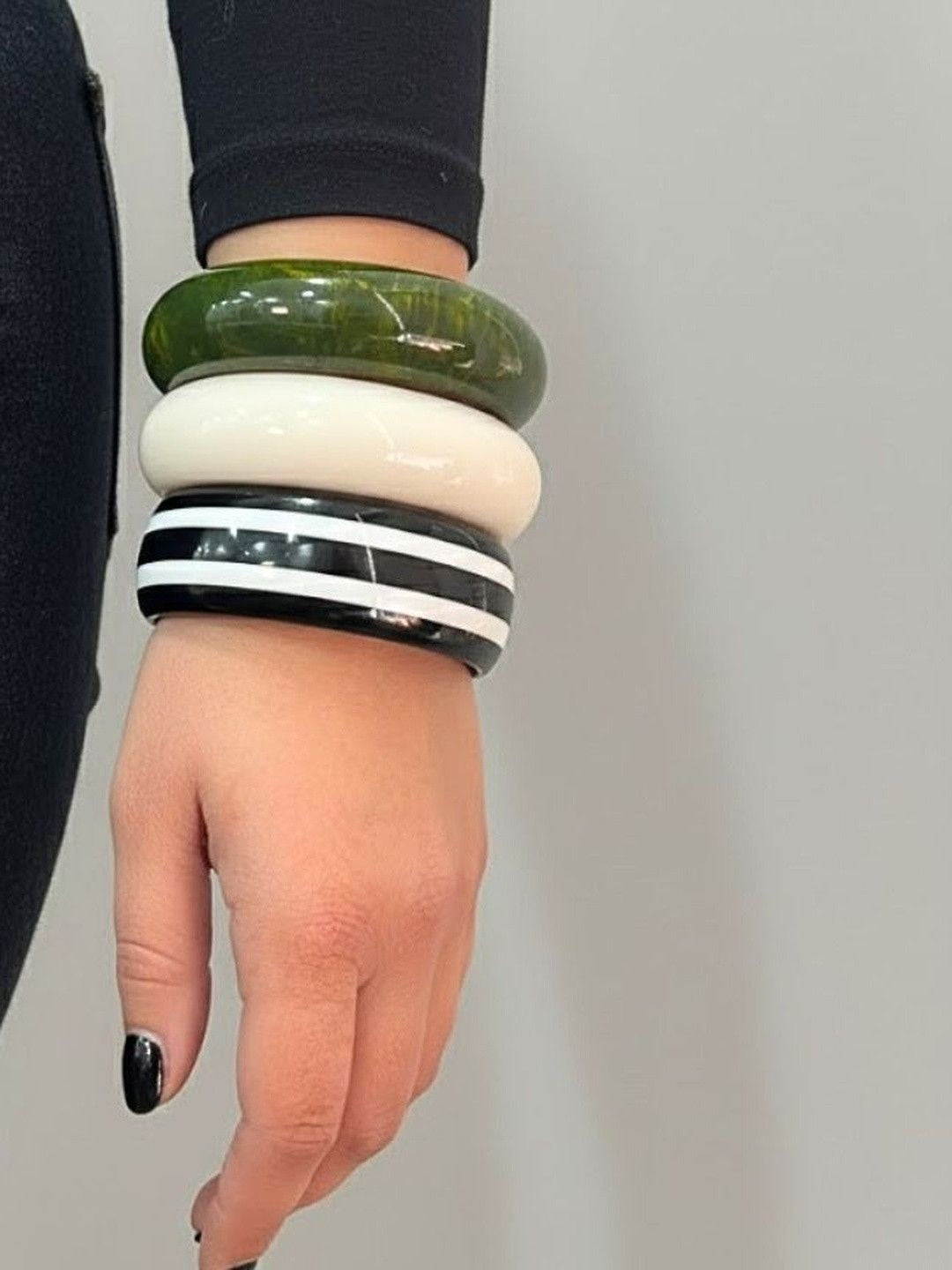 Three stacked resin bangles on a woman's wrist — green marble, ivory, and black-and-white stripe