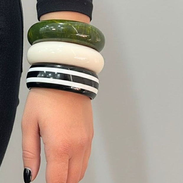 Three stacked resin bangles on a woman's wrist — green marble, ivory, and black-and-white stripe