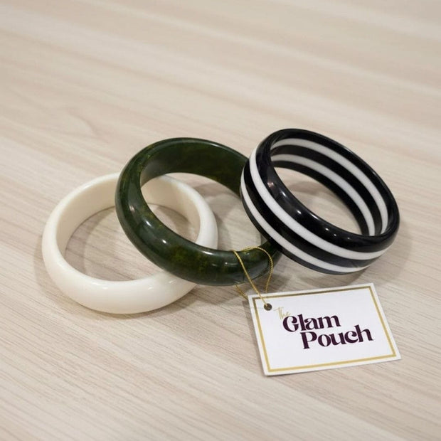 Three resin bangles laid flat on a wooden surface beside a Glam Pouch brand tag