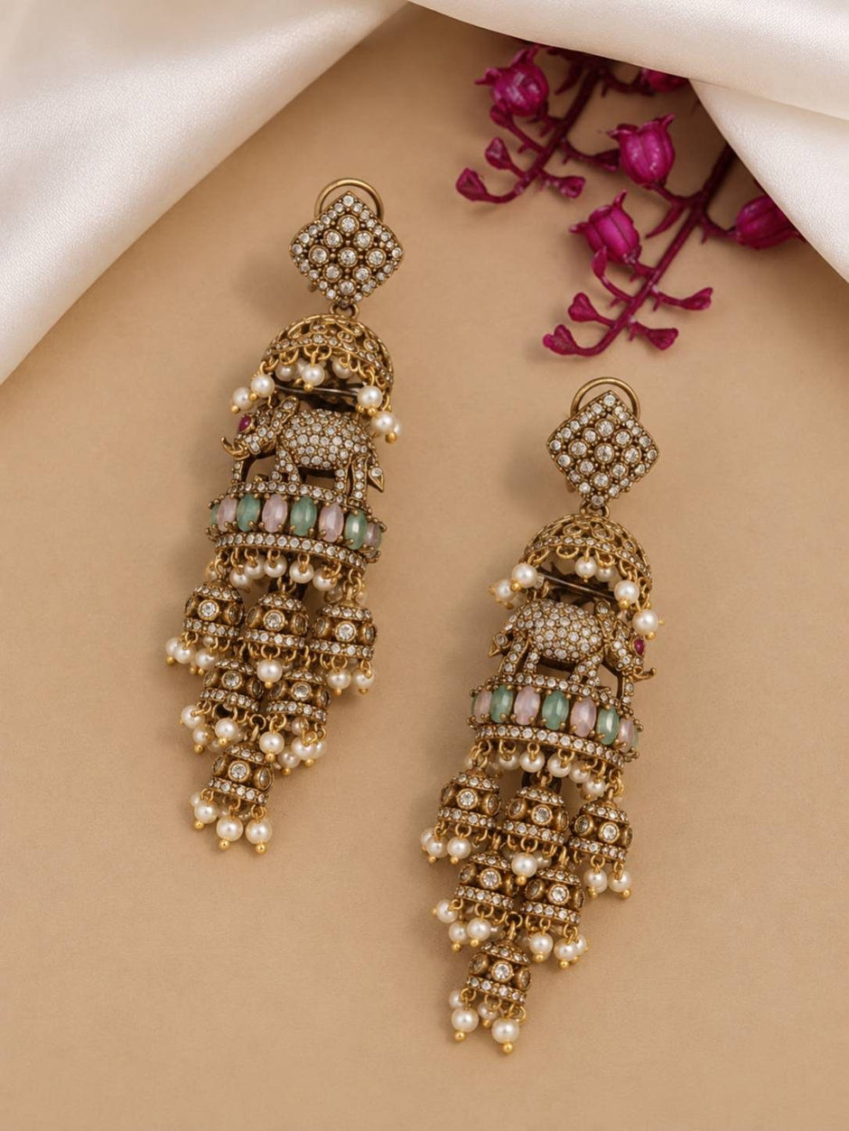 Two oxidised gold elephant jhumka earrings laid flat on a beige surface showing full front detail with crystal embellishments and pearl drops