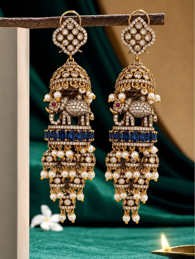 Pair of oxidised gold elephant jhumka earrings with blue sapphire band and pearl drops displayed on a metal stand against green drape