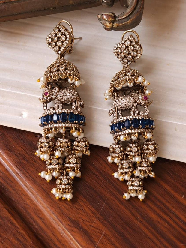 Front view of oxidised gold elephant jhumka earrings laid flat on a white marble surface showing full layered design