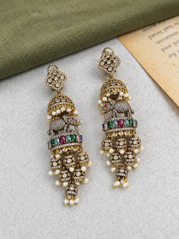 Two antique gold jhumka earrings laid flat showing front face with pearl drops and coloured stones