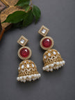 Pair of gold-plated kundan ruby jhumka earrings with pearl fringe displayed on grey surface