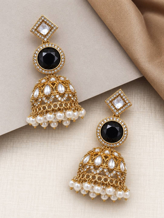 Pair of gold-plated black stone kundan jhumkas laid flat on cream surface showing front detail